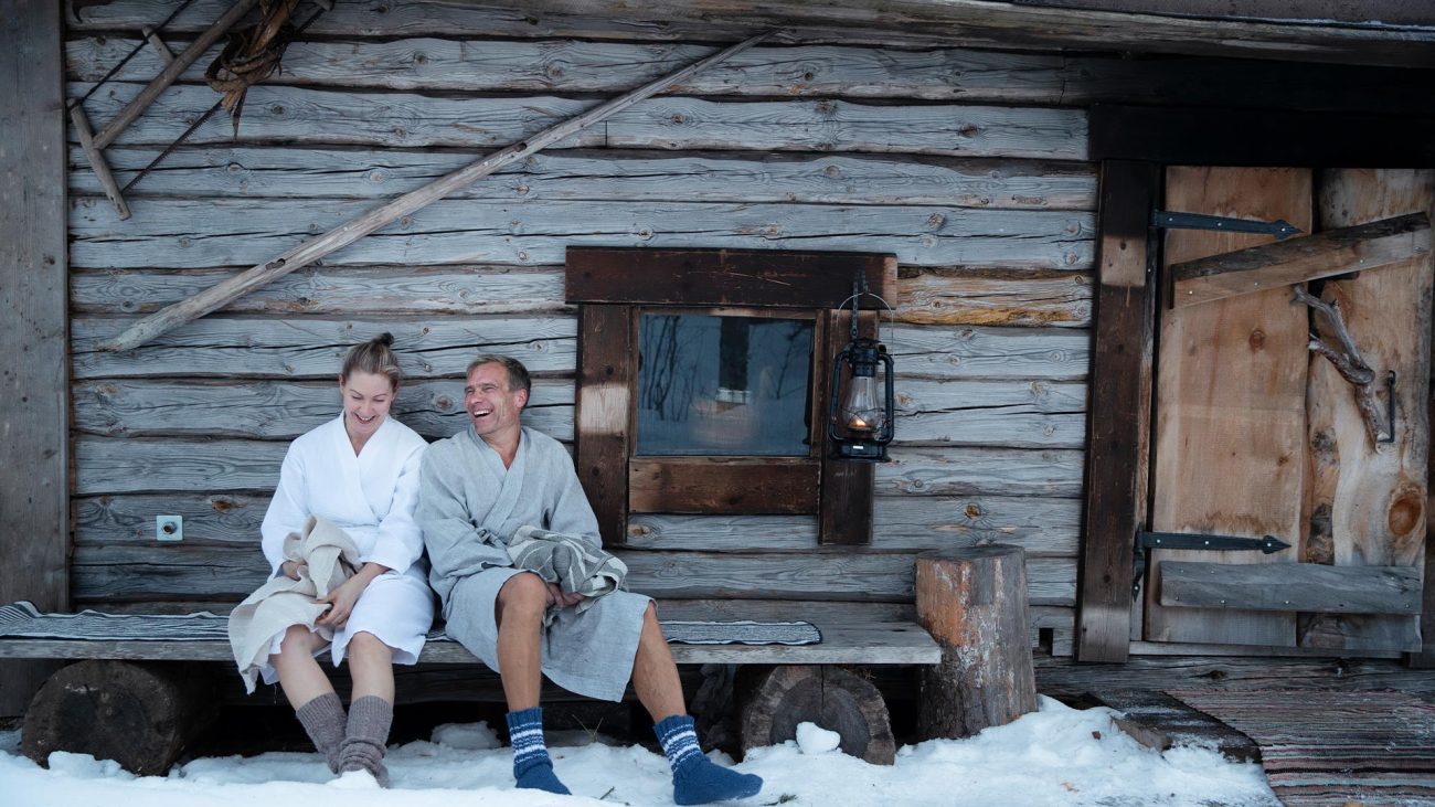 Zwei glückliche Menschen sitzen vor einer finnischen Sauna im Winter. 