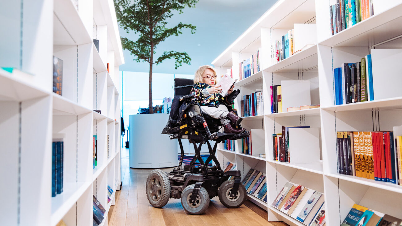 Eine Frau im Rollstuhl liest ein Buch in der Oodi-Bibliothek in Finnland.