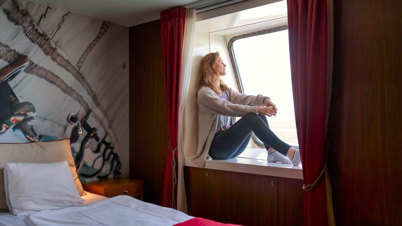 Frau sitzt im Kabinenfenster und blickt nach draußen. 