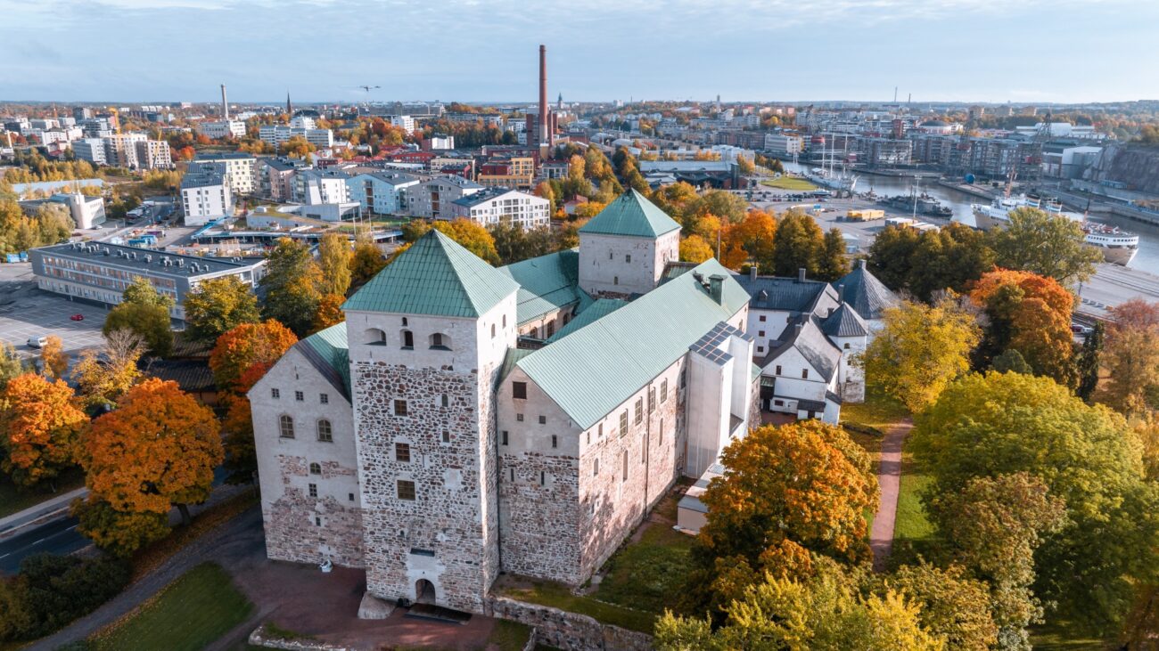 Die Burg Turku, umgeben von herbstlich gefärbten Bäumen, mit der Stadt und dem Fluss Aura im Hintergrund.