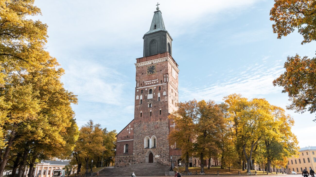 Der Dom von Turku, umgeben von herbstlich gefärbten Bäumen, mit seinem markanten, hohen Turm, der sich gegen den blauen Himmel abhebt.