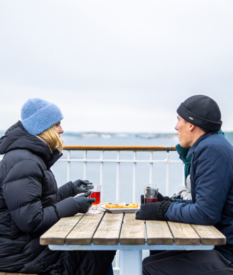 Bild på ett par i vinterkläder och som dricker varmt te och fikar ute på däck. 