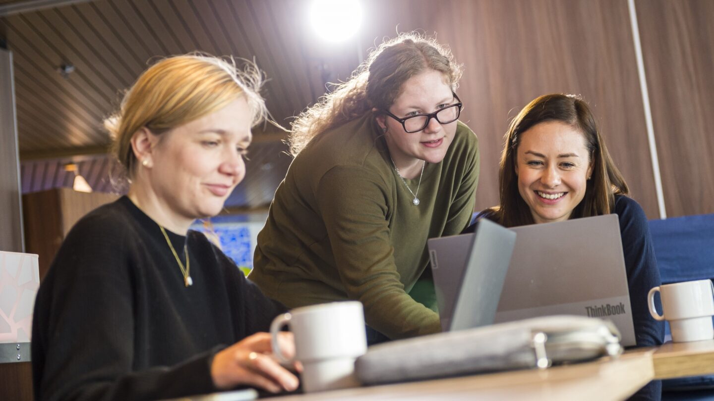 Frauen in Tagungsraum blicken gemeinsam auf Laptop. 