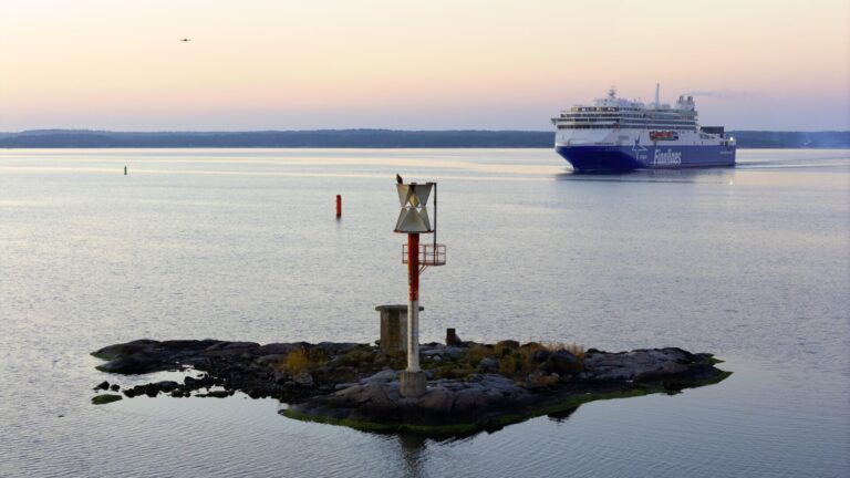 Finnlines' vessel Finnsirius approaching port during a calm evening; in the foreground, a small islet with a navigation marker and a perched seabird