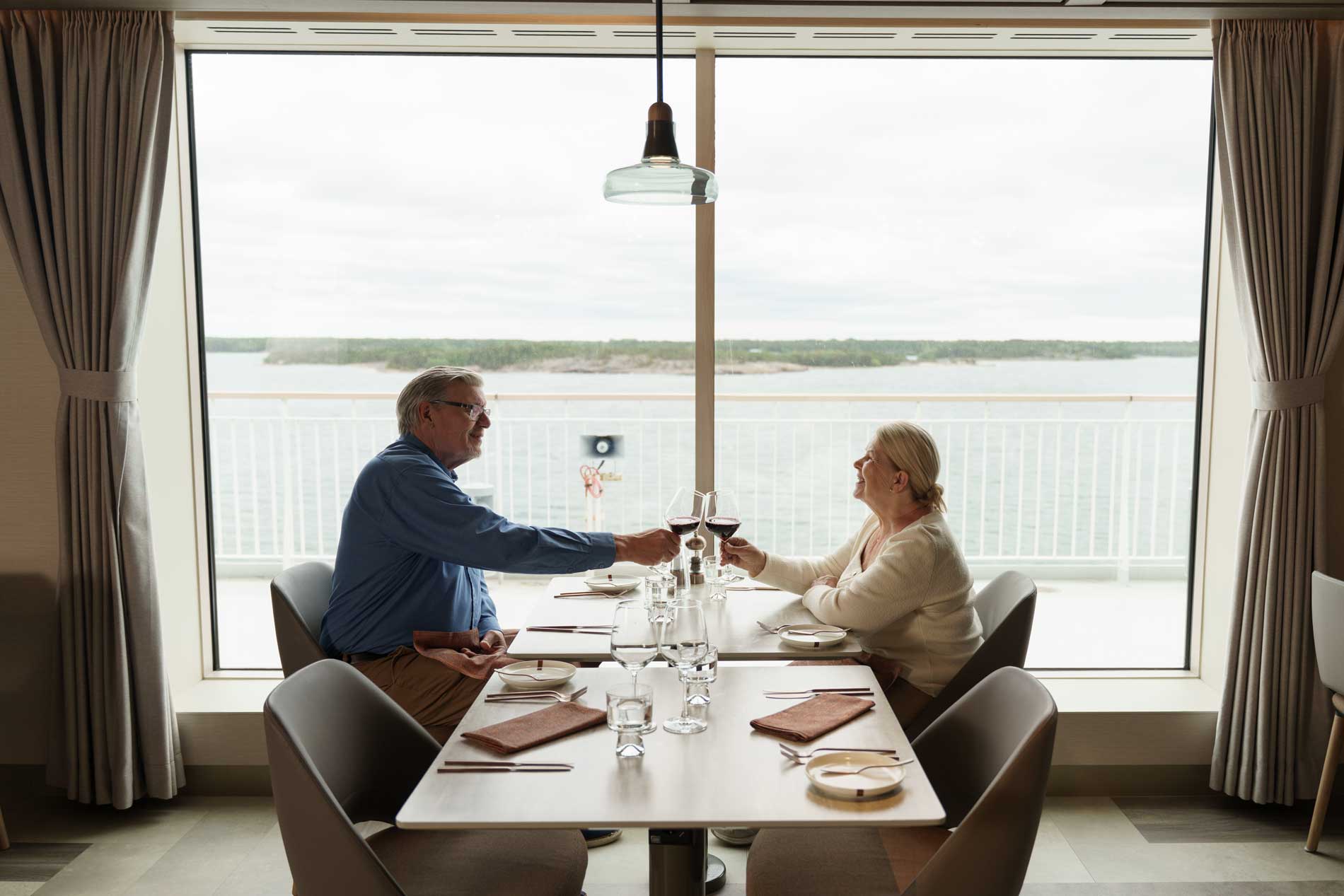 Bild på ett äldre par som äter middag och skålar i vinglas över bordet, ombord på Finnlines fartyg.