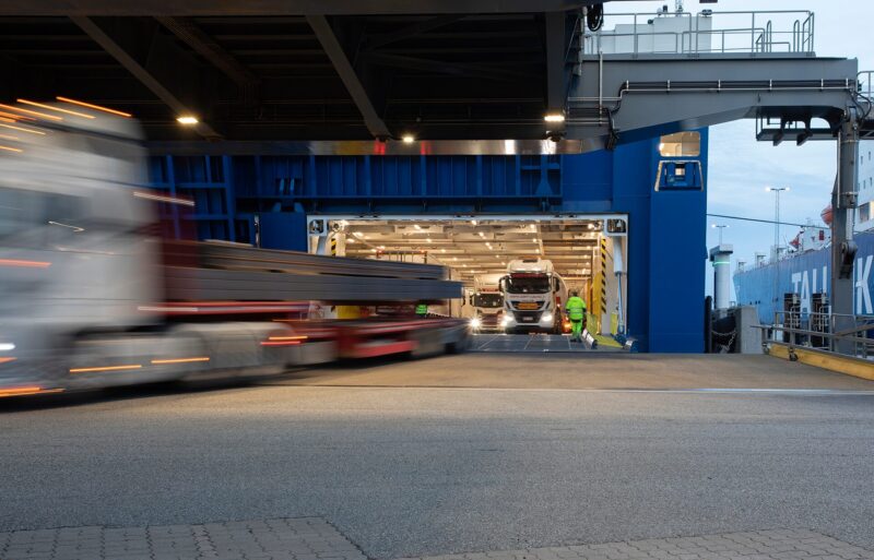 Port scene showing trucks moving on and off a cargo ship, illustrating digital transformation in port operations.