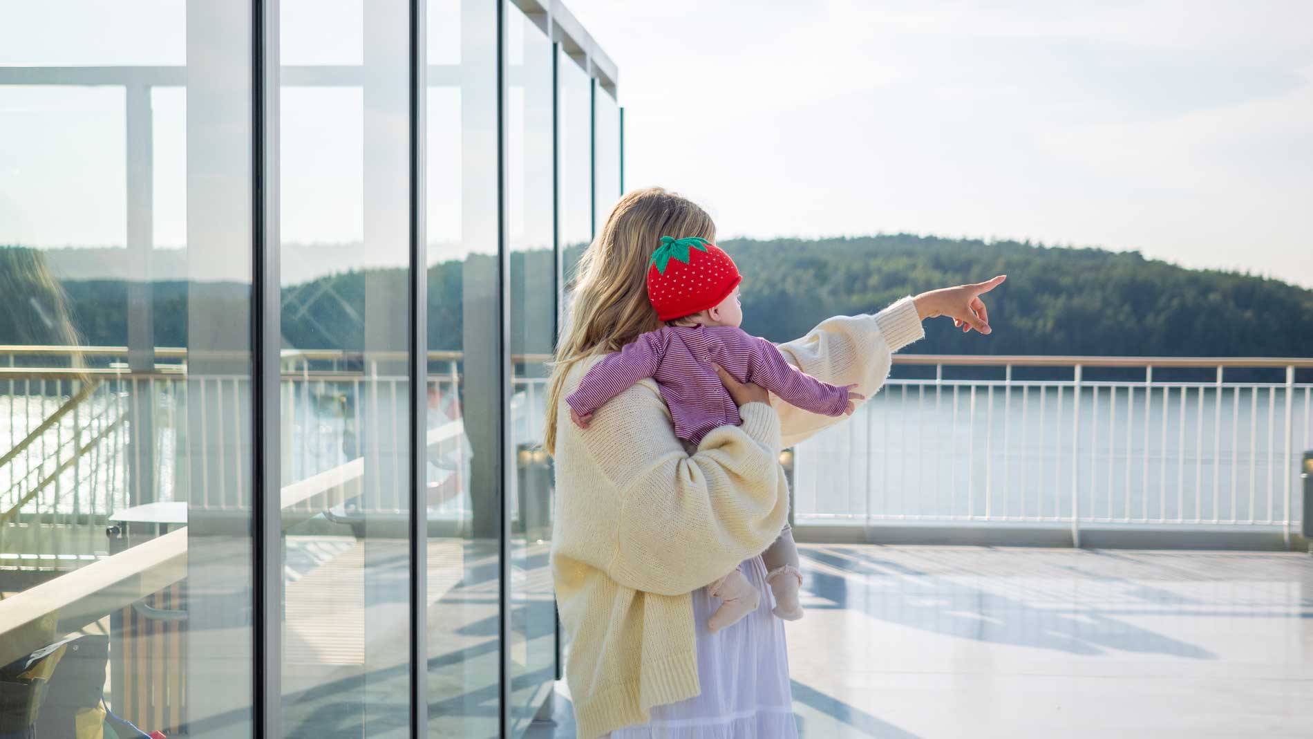 Bild på en blond tjej som håller sin bebis i famnen och pekar ut mot skärgården.