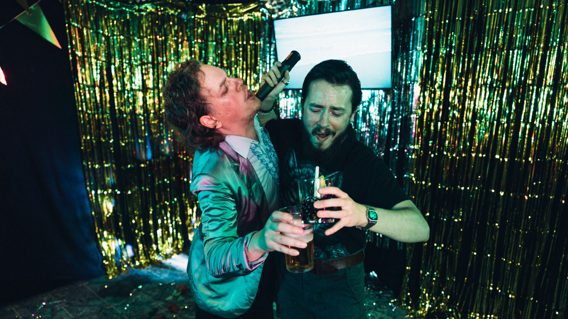 Bild på två överförfriskade män som sjunger karaoke med varsin drink i handen.